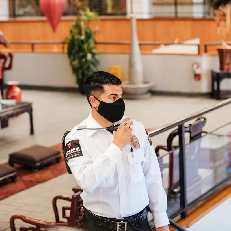 A security guard in a white uniform and face mask delivering professional security services inside a commercial building