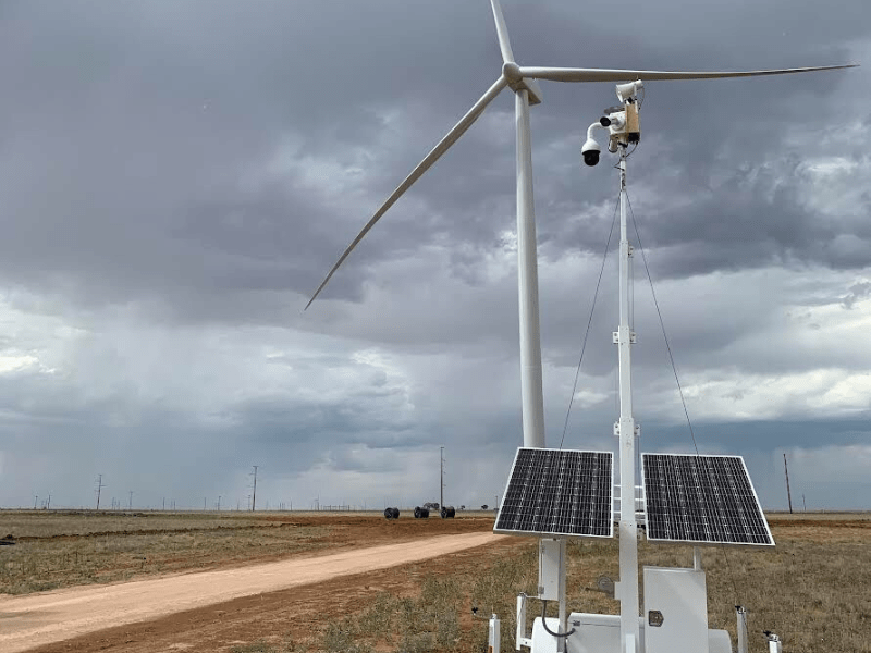 A Superior Protection Services Mobile Surveillance Unit mounted with solar panels on a remote field with a dirt road under a cloudy sky.