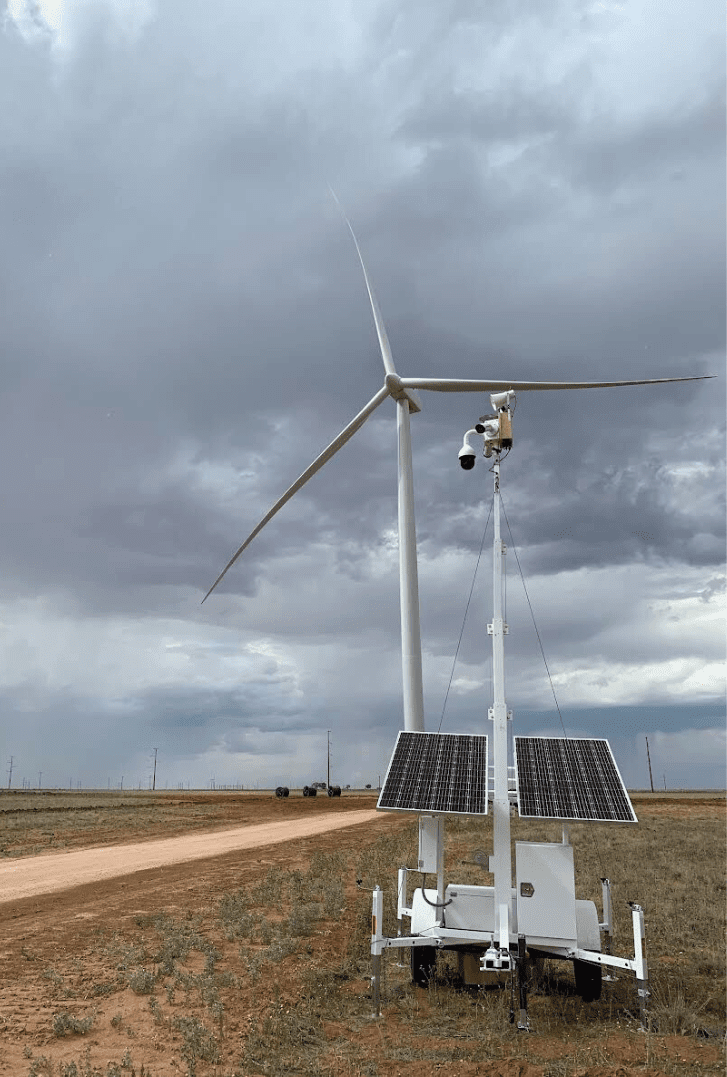 A Superior Protection Services Mobile Surveillance Unit mounted with solar panels on a remote field with a dirt road under a cloudy sky.